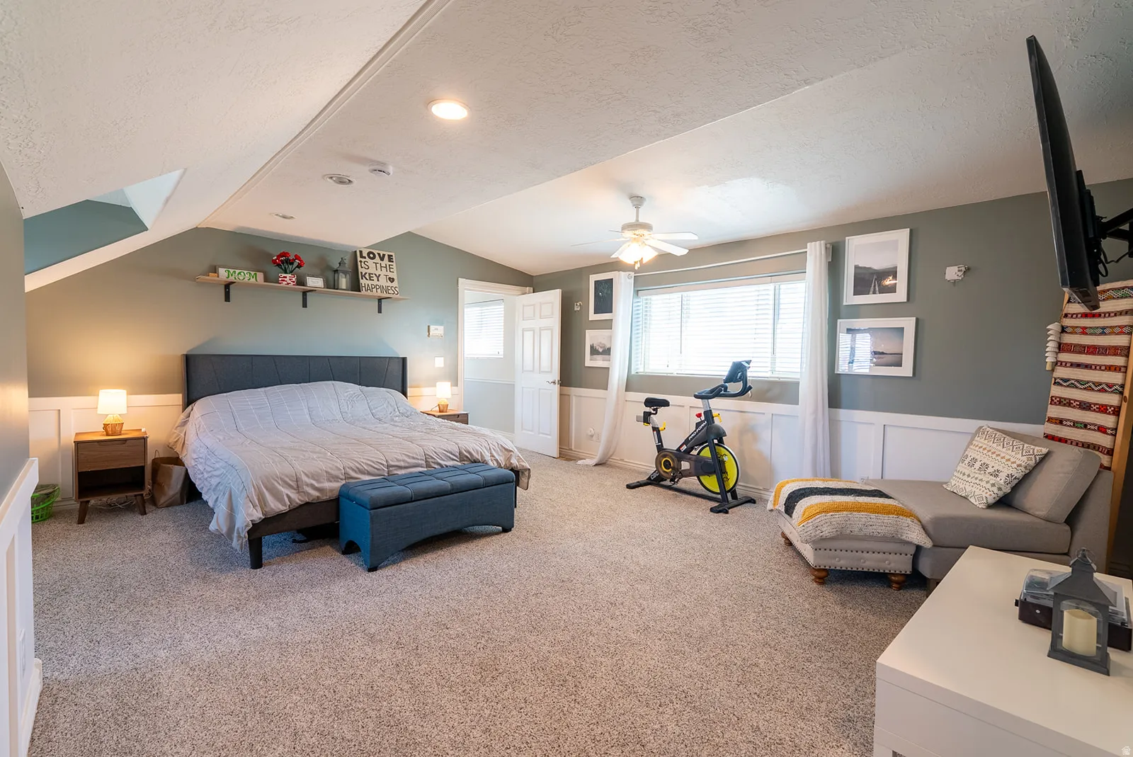 Carpeted bedroom featuring a wainscoted wall, a decorative wall, and a ceiling fan