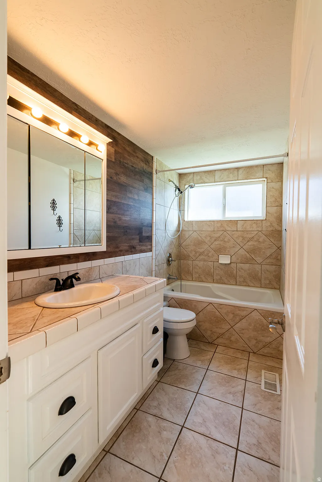 Full bathroom featuring vanity, tiled shower / bath combo, light tile patterned flooring, a textured ceiling, and tile walls