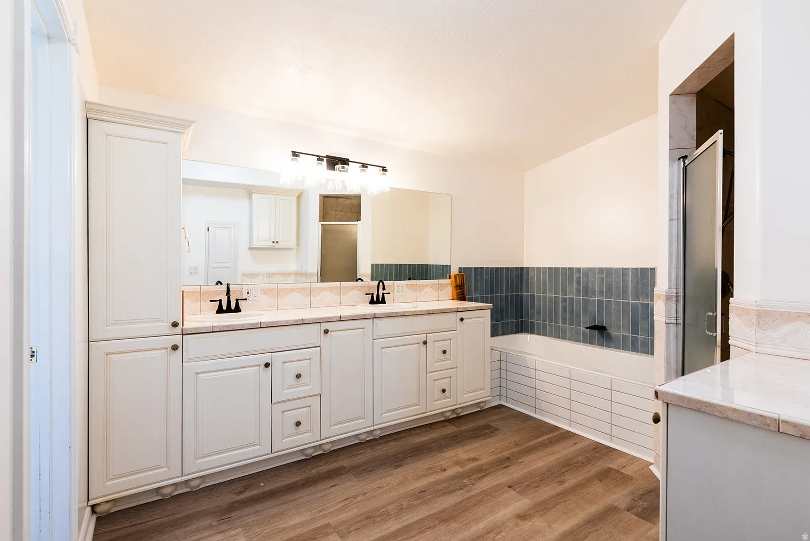 Full bath with double vanity, a garden tub, a stall shower, and wood finished floors