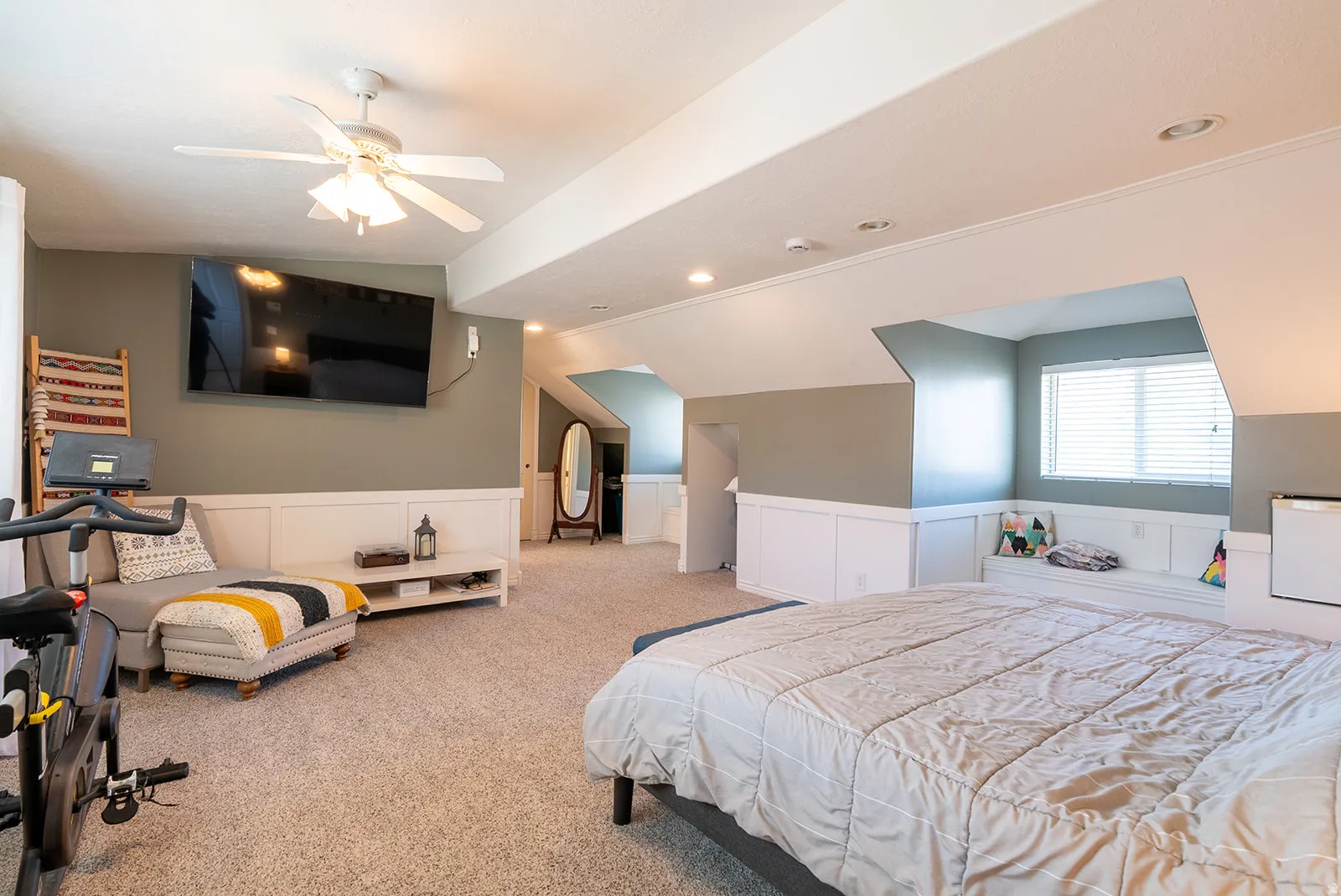 Bedroom featuring wainscoting, a decorative wall, light carpet, lofted ceiling, and a ceiling fan