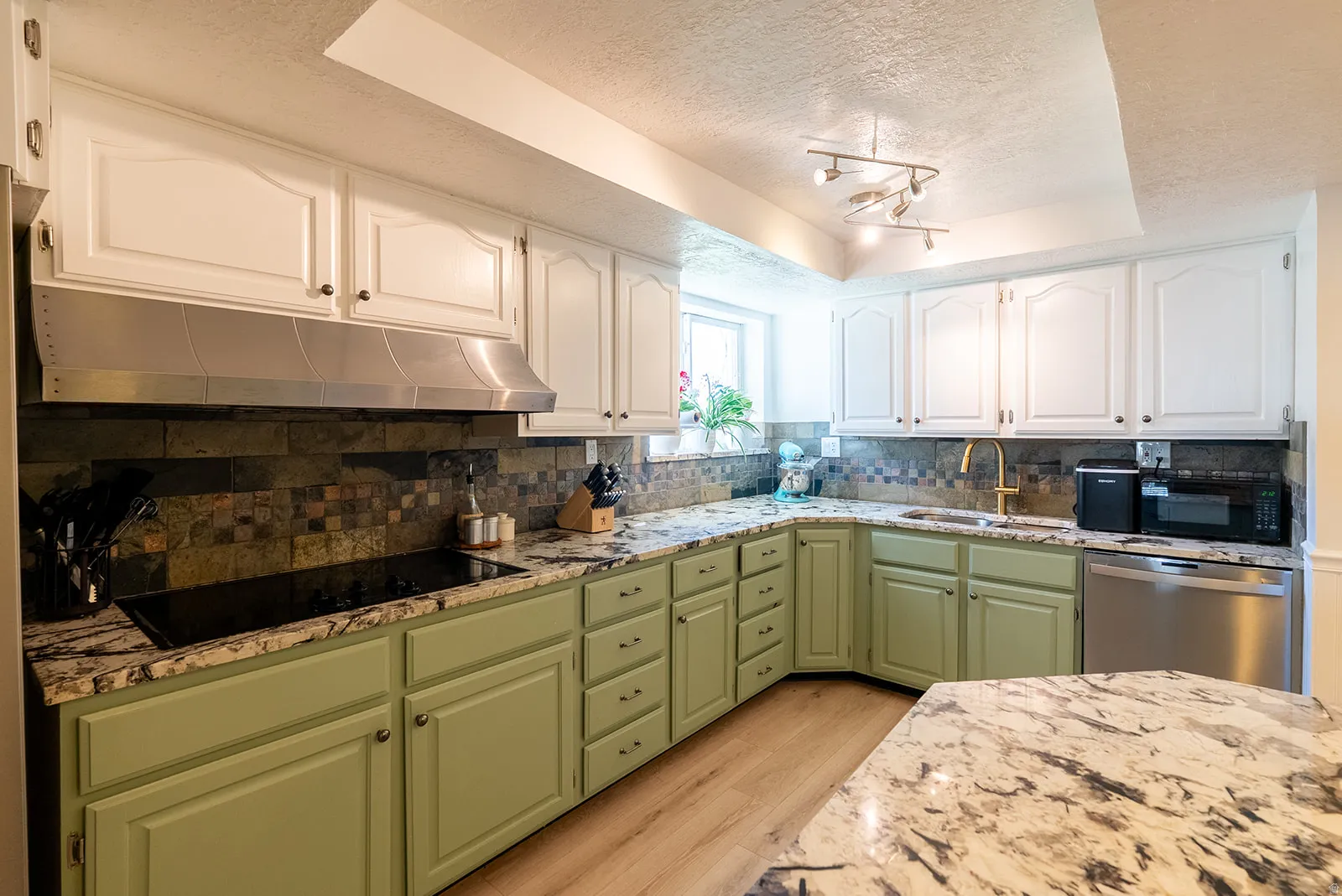 Kitchen featuring two tone color scheme, a textured ceiling, light stone counters, a tray ceiling, and light wood-type flooring
