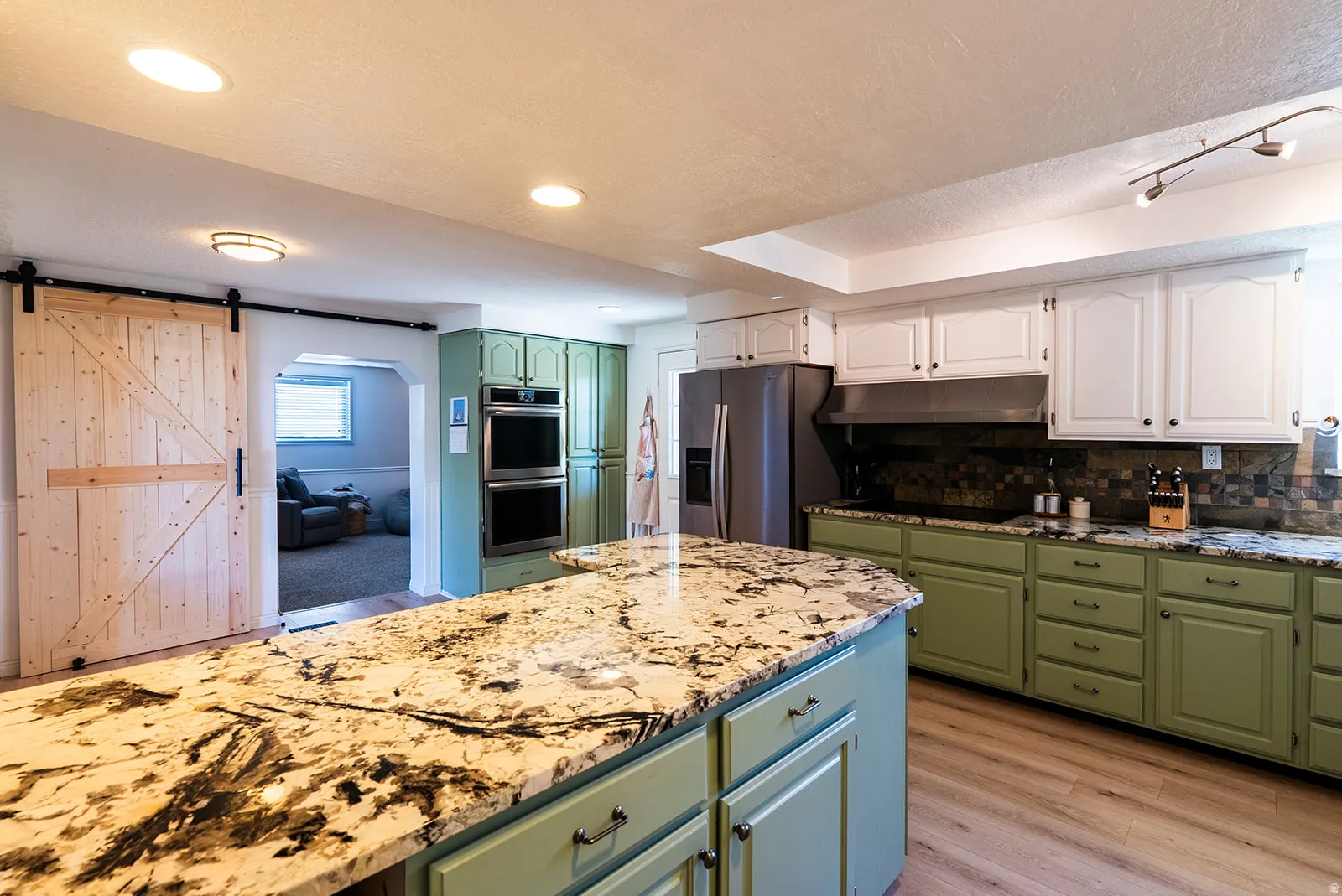 Two tone kitchen featuring two tone cabinets, a barn door, light stone countertops, light wood-type flooring, and tasteful backsplash