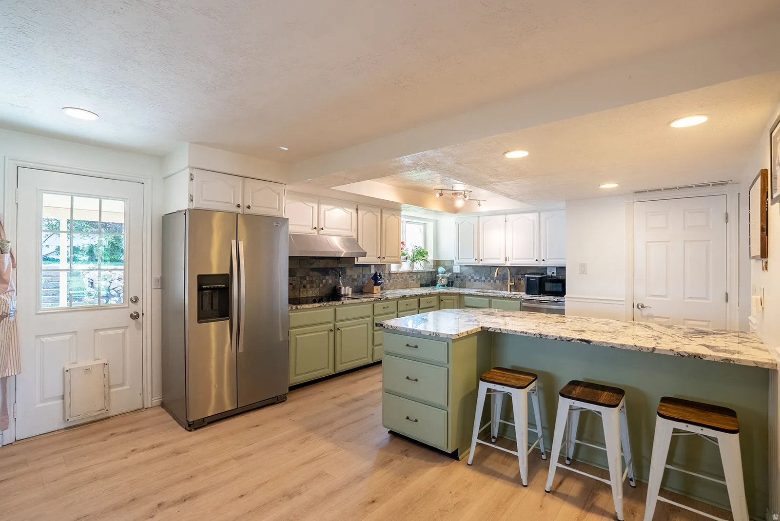 Kitchen featuring two tone cabinets, a breakfast bar area, black appliances, light wood-style flooring, and light stone counters