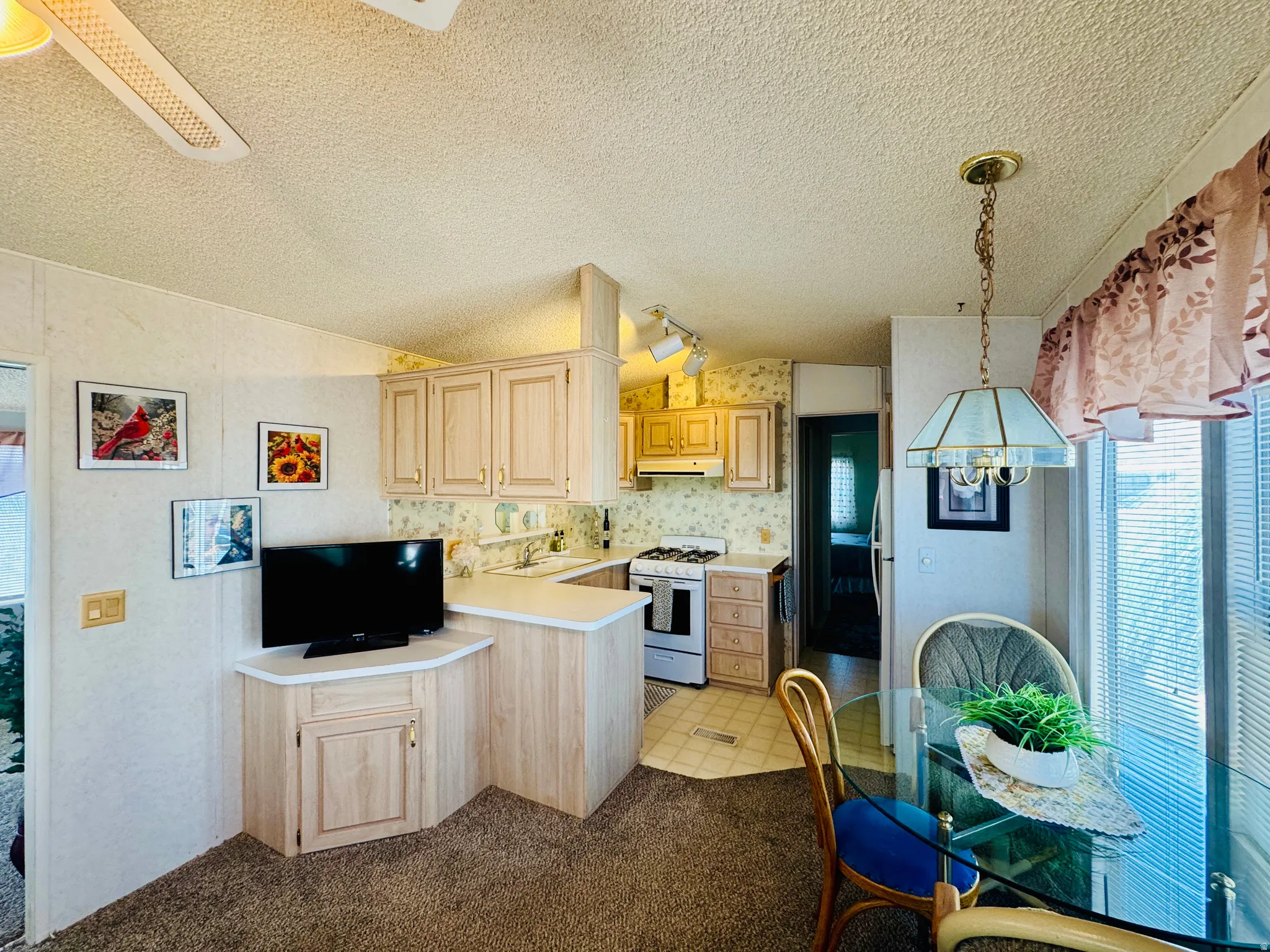 Kitchen with light wood finish cabinets, light countertops, white range with gas cooktop, wallpapered walls, and a textured ceiling