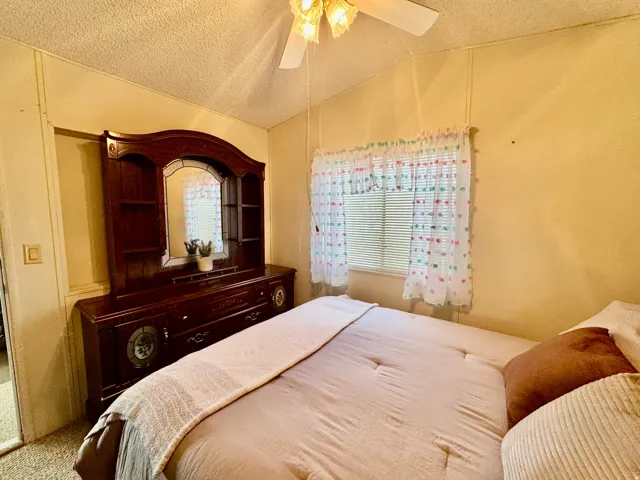 Carpeted bedroom featuring ceiling fan, a textured ceiling, and a textured wall