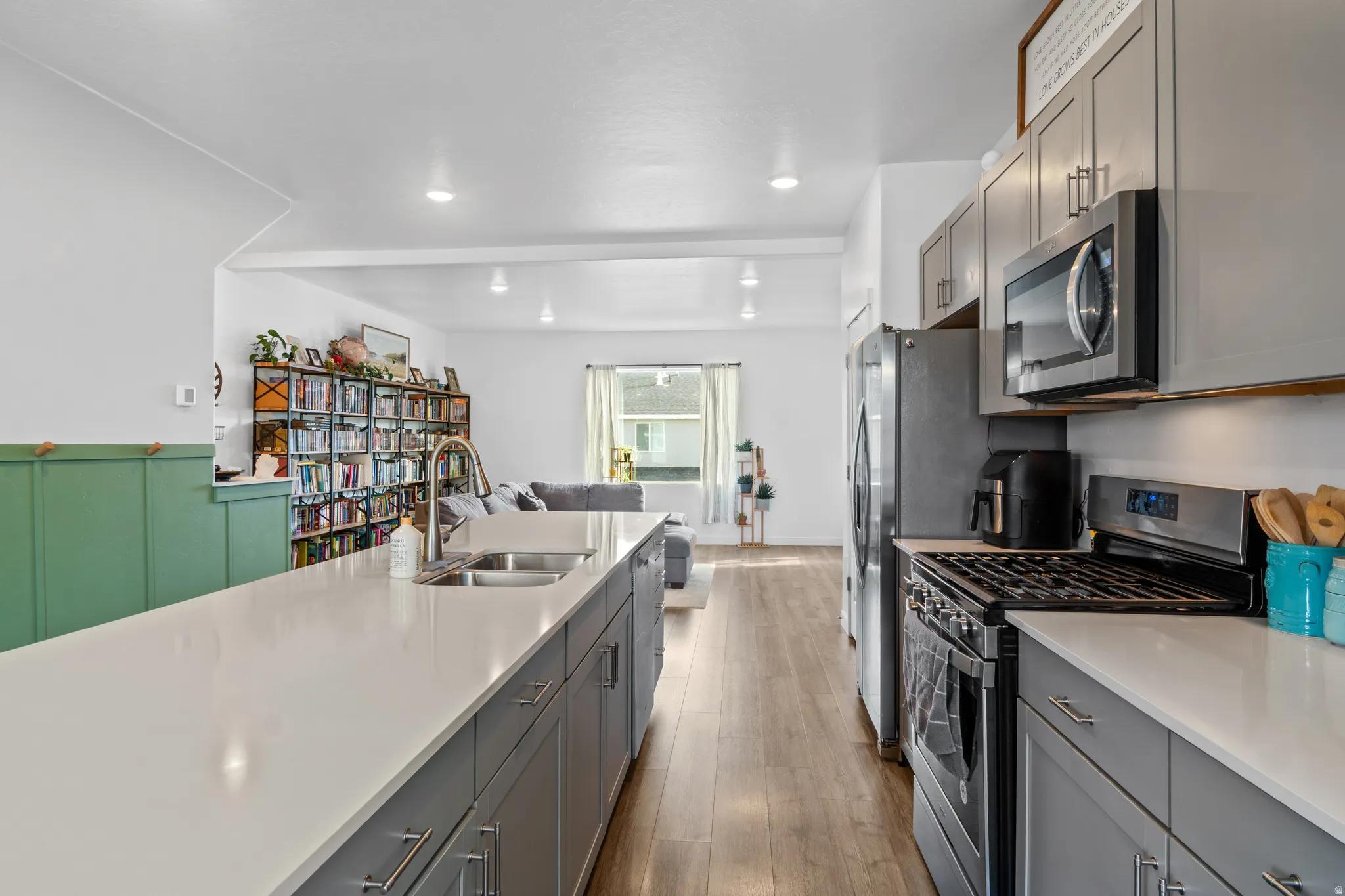 Kitchen featuring stainless steel appliances, gray cabinetry, open floor plan, light wood-style flooring, and light stone counters