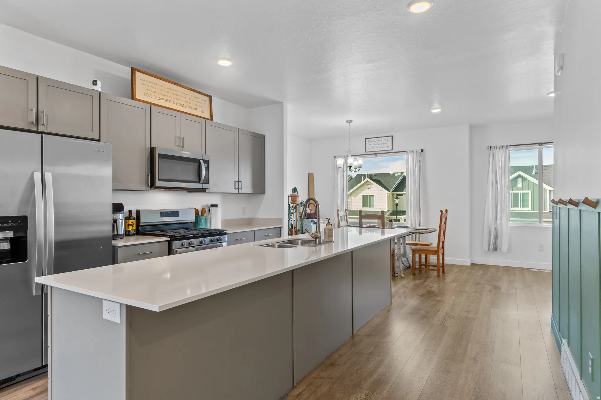 Kitchen featuring gray cabinets, stainless steel appliances, an island with sink, light wood-style floors, and suspended lighting