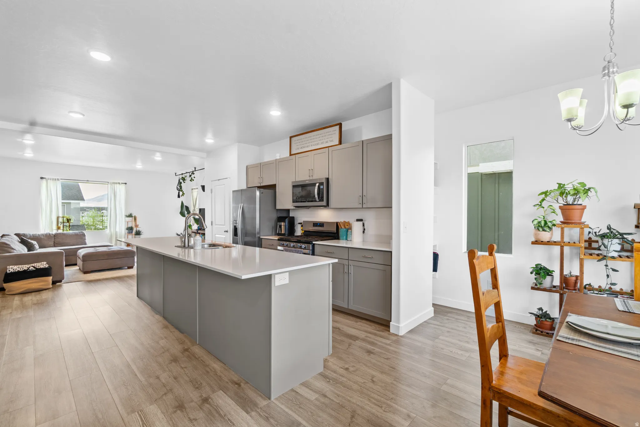 Kitchen featuring open floor plan, gray cabinets, stainless steel appliances, a quartz island with sink, and light wood-type flooring