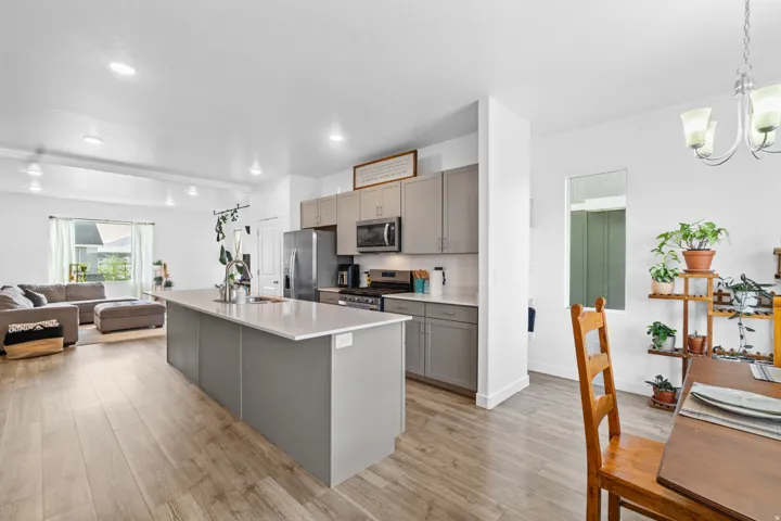 Kitchen featuring open floor plan, gray cabinets, stainless steel appliances, a quartz island with sink, and light wood-type flooring