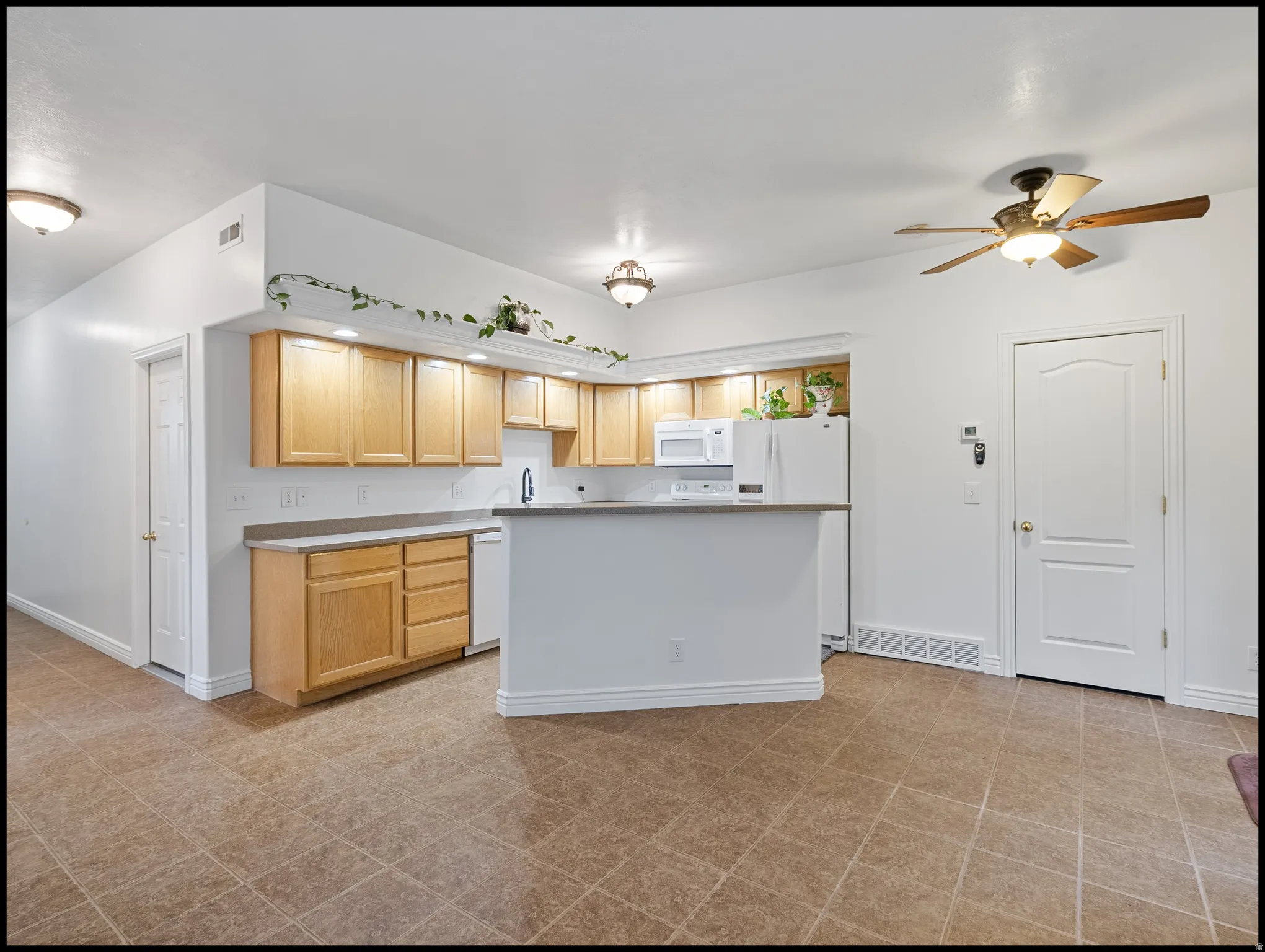 Kitchen with light wood finish cabinets, light countertops, ceiling fan, white appliances, and a kitchen island