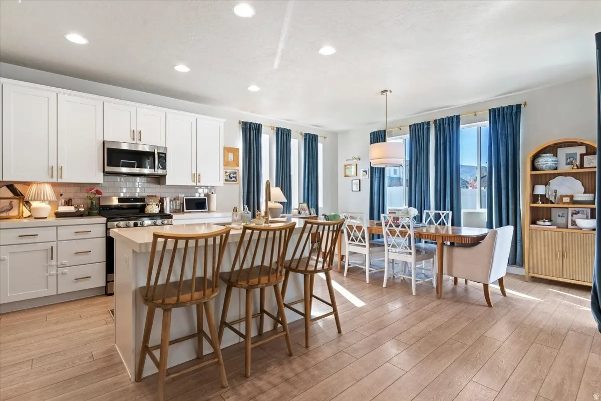 Kitchen featuring light countertops, stainless steel appliances, a center island with sink, a breakfast bar area, and light wood-style floors