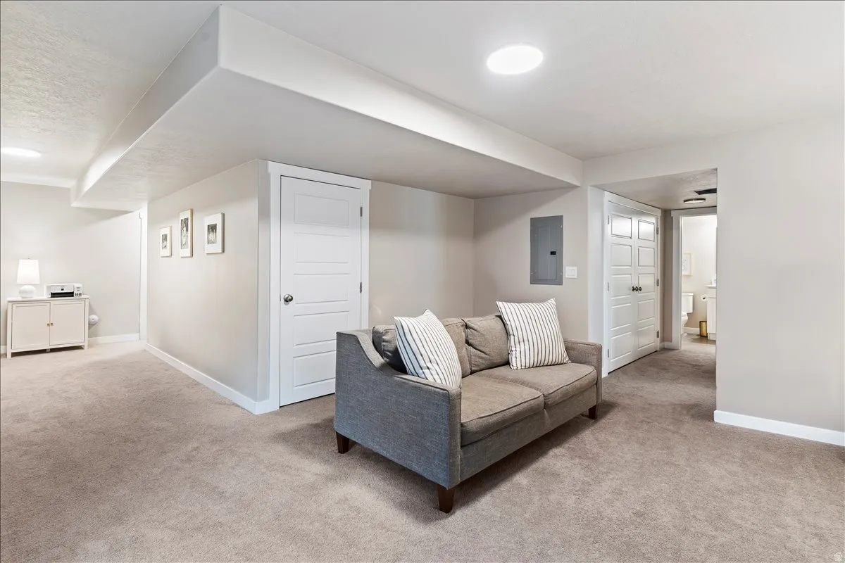 Living area with light colored carpet, electric panel, and a textured ceiling