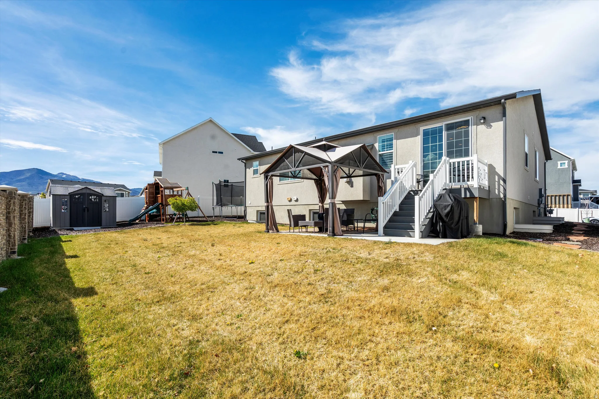 Back of property with a patio, a storage unit, a gazebo, a fenced backyard, and a playground