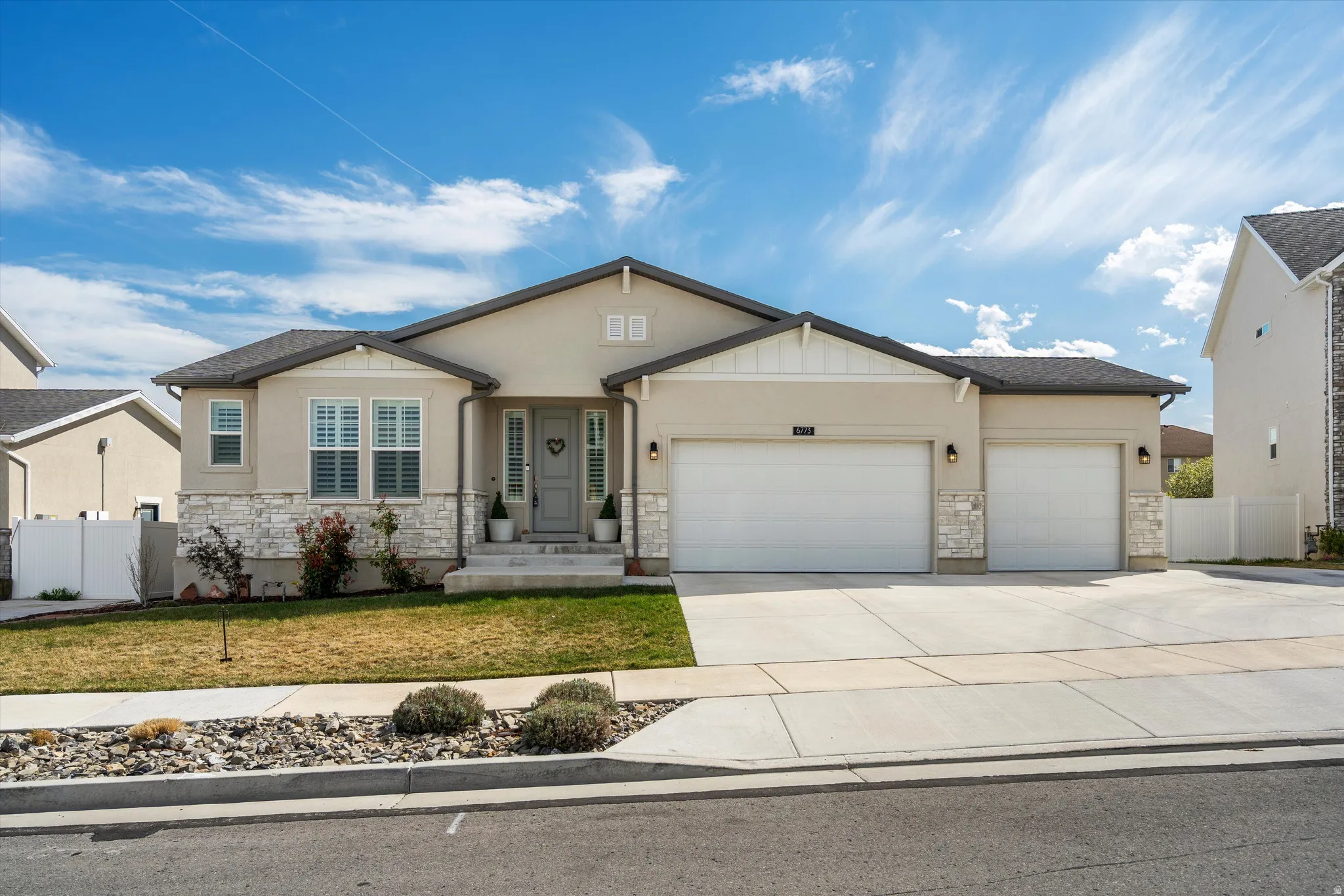 View of front of house with an attached garage, stone siding, driveway, and stucco siding