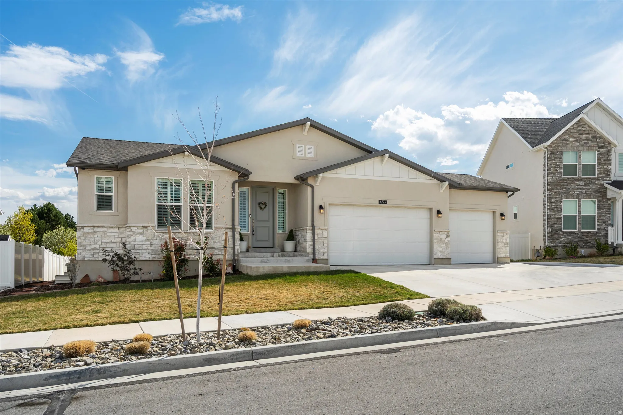 View of front facade with an attached garage, a front yard, stone siding, driveway, and stucco siding