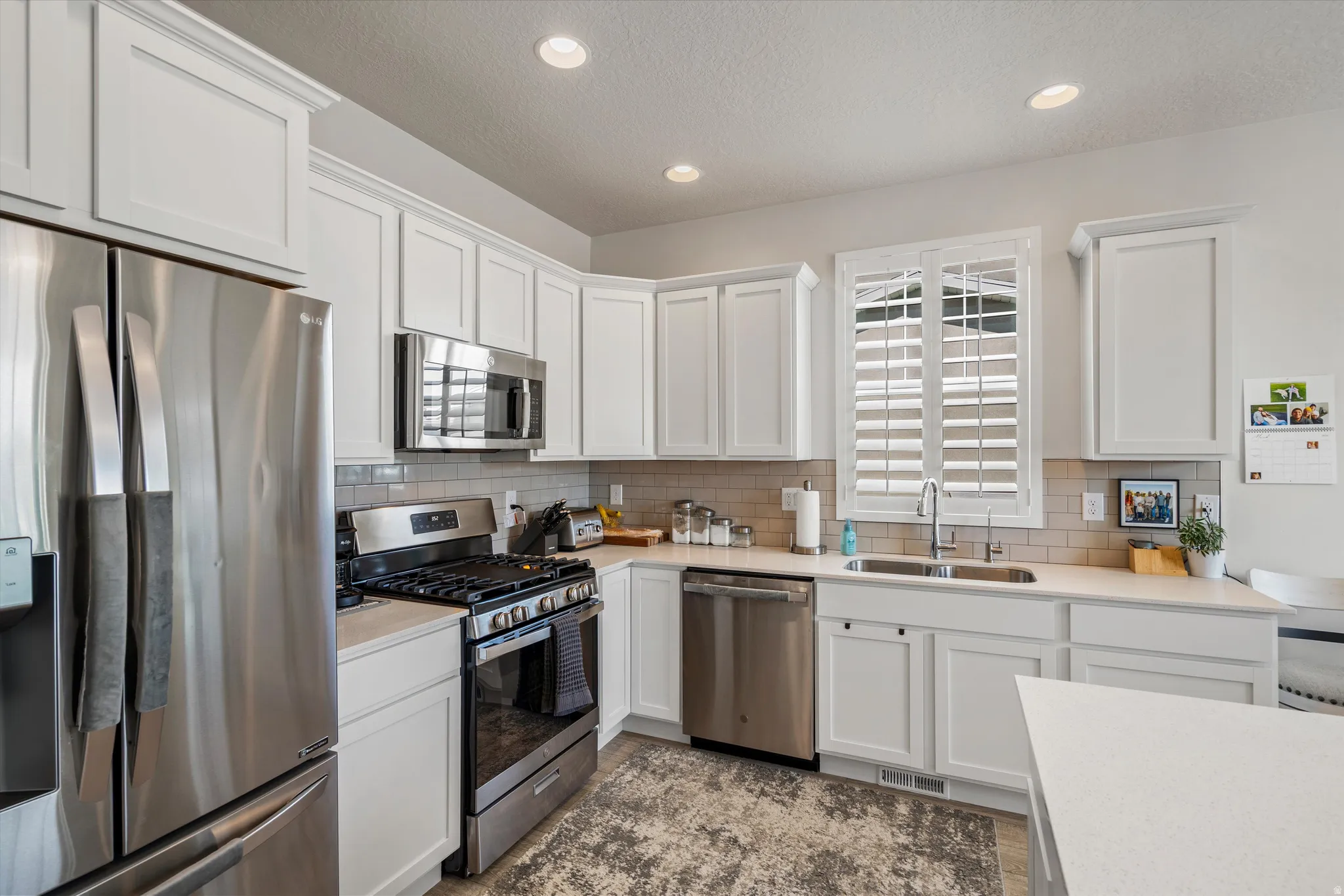 Kitchen with stainless steel appliances, white cabinets, recessed lighting, tasteful backsplash, and light stone counters