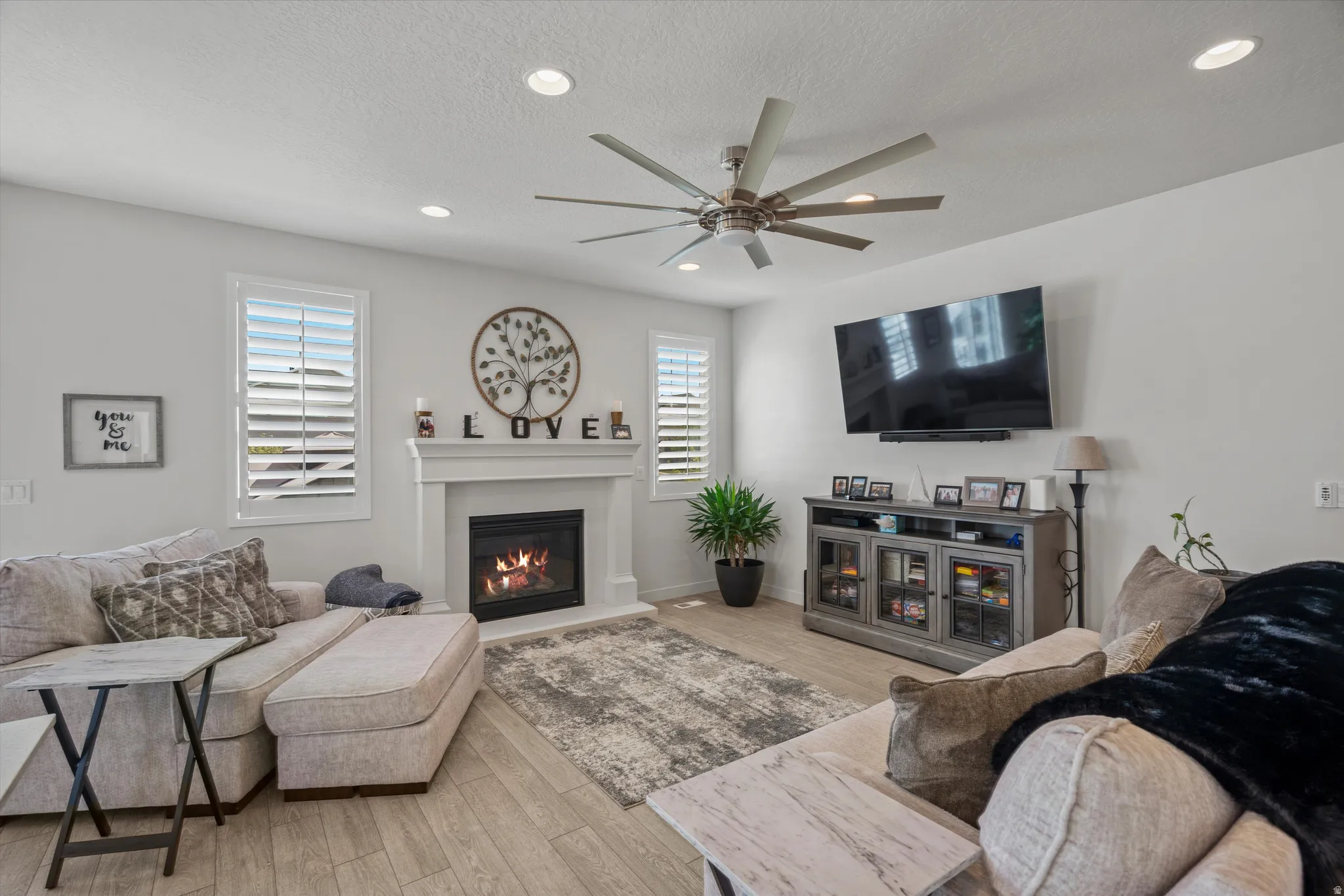 Living area with light wood-type flooring, recessed lighting, a glass covered fireplace, a ceiling fan, and a textured ceiling