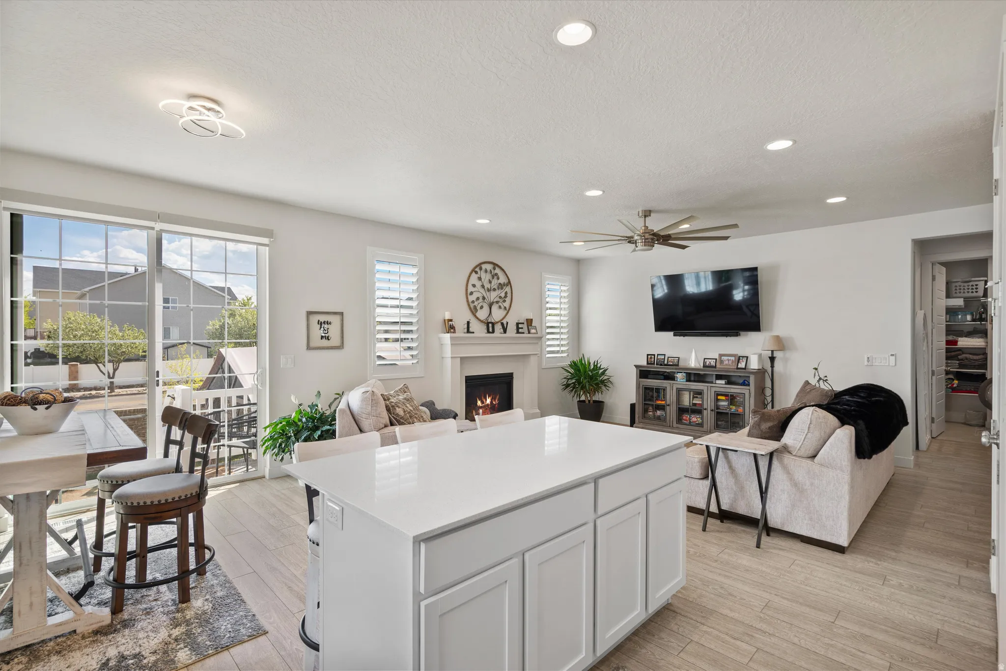 Living area with light wood-style floors, ceiling fan, a lit fireplace, recessed lighting, and a textured ceiling