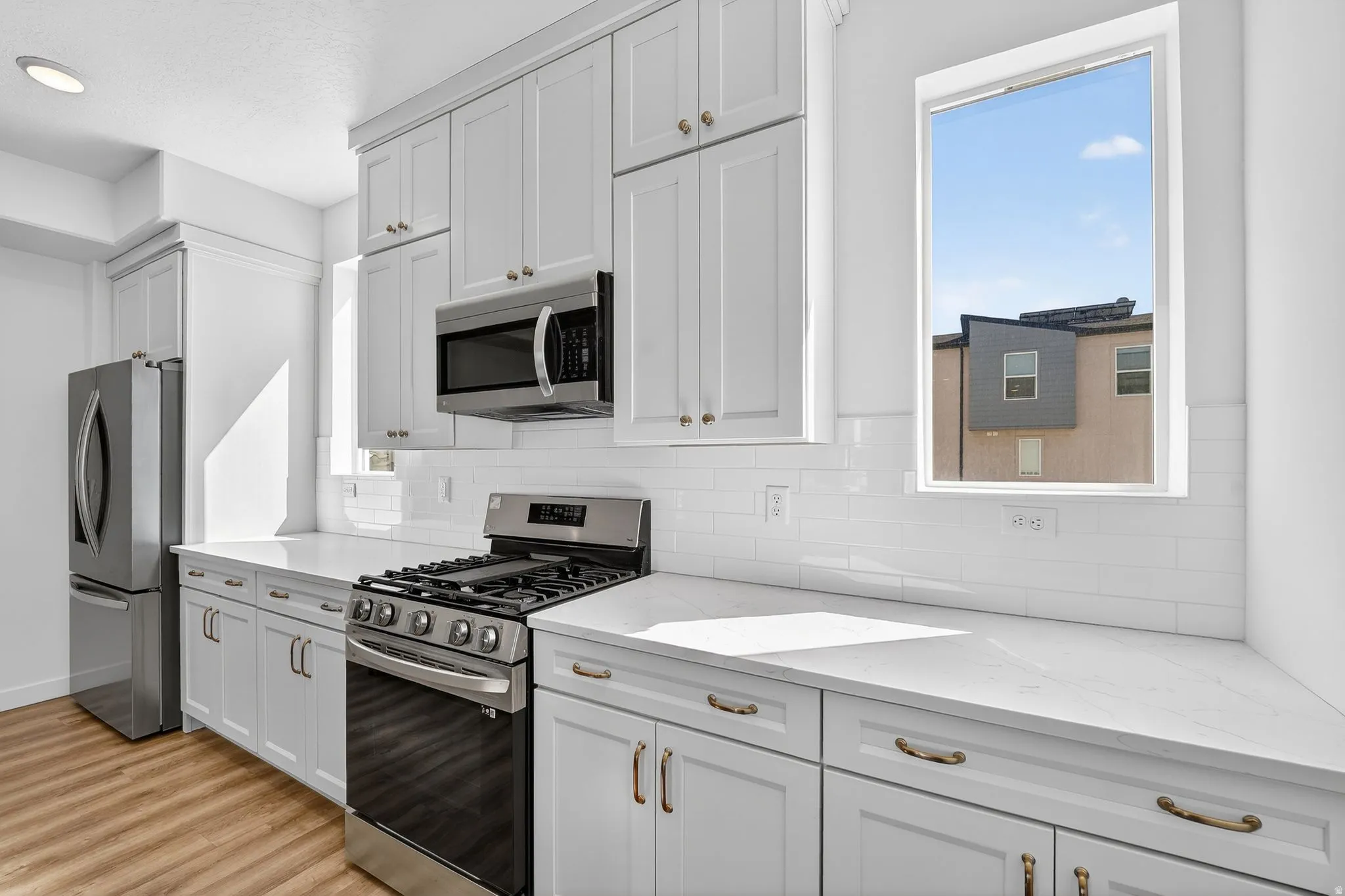 Kitchen featuring stainless steel appliances, white cabinets, light stone counters, backsplash, and light wood-style flooring