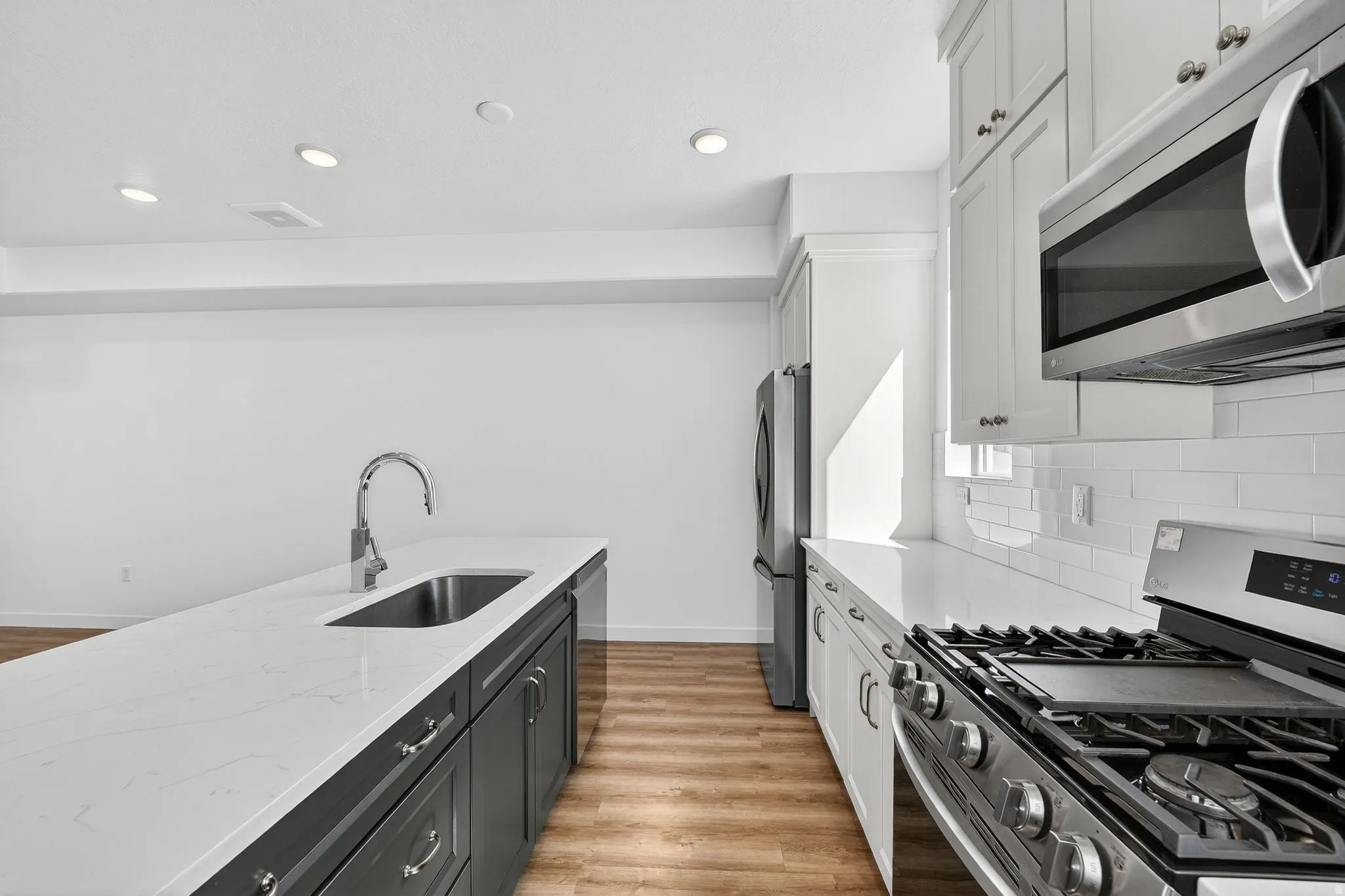 Kitchen featuring stainless steel appliances, dual tone cabinetry, light stone counters, light wood finished floors, and recessed lighting