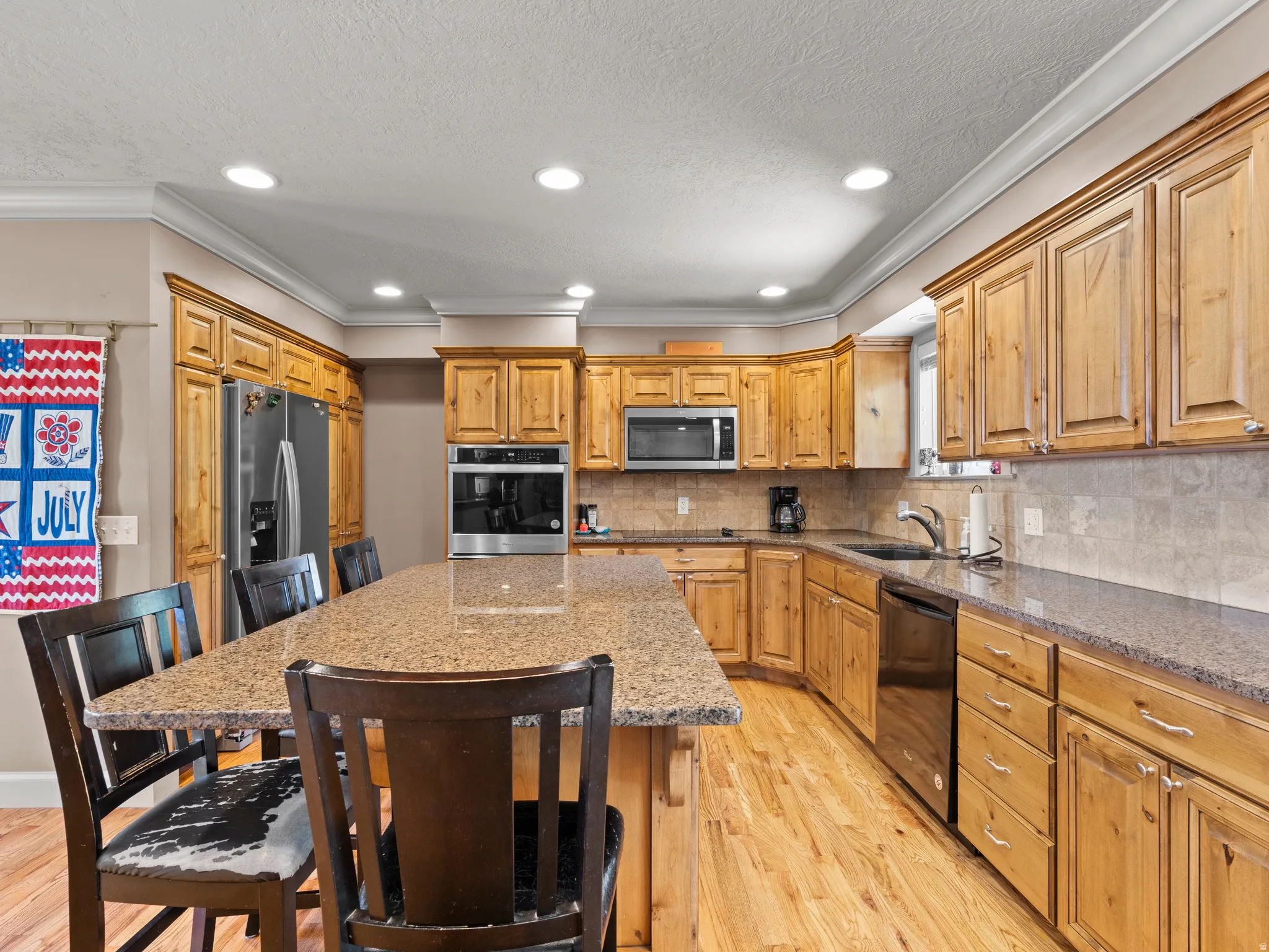 Kitchen with a kitchen island, light wood-type flooring, a breakfast bar, black appliances, and dark stone countertops