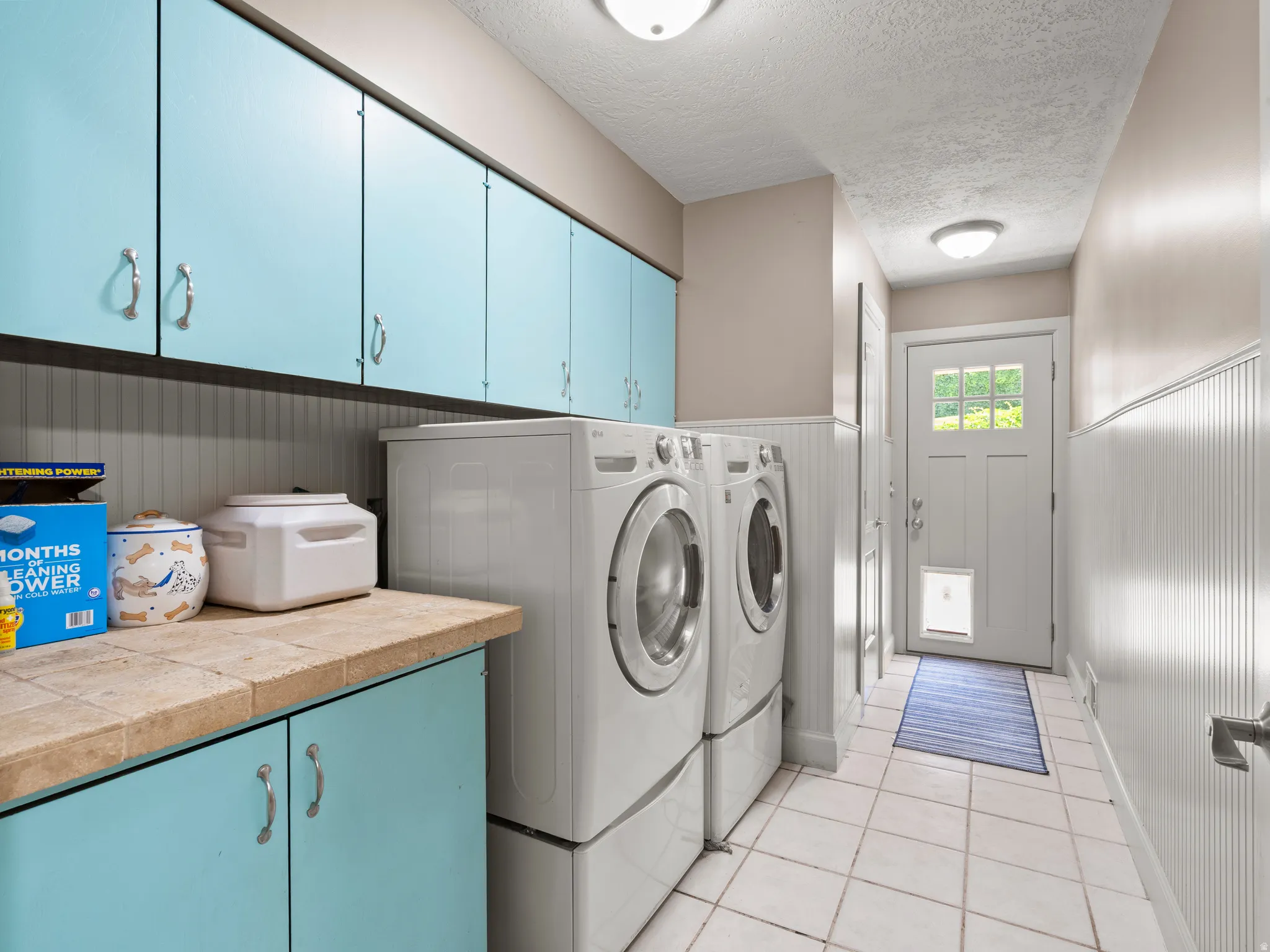 Laundry area featuring a wainscoted wall, cabinet space, a textured ceiling, light tile patterned floors, and washing machine and clothes dryer