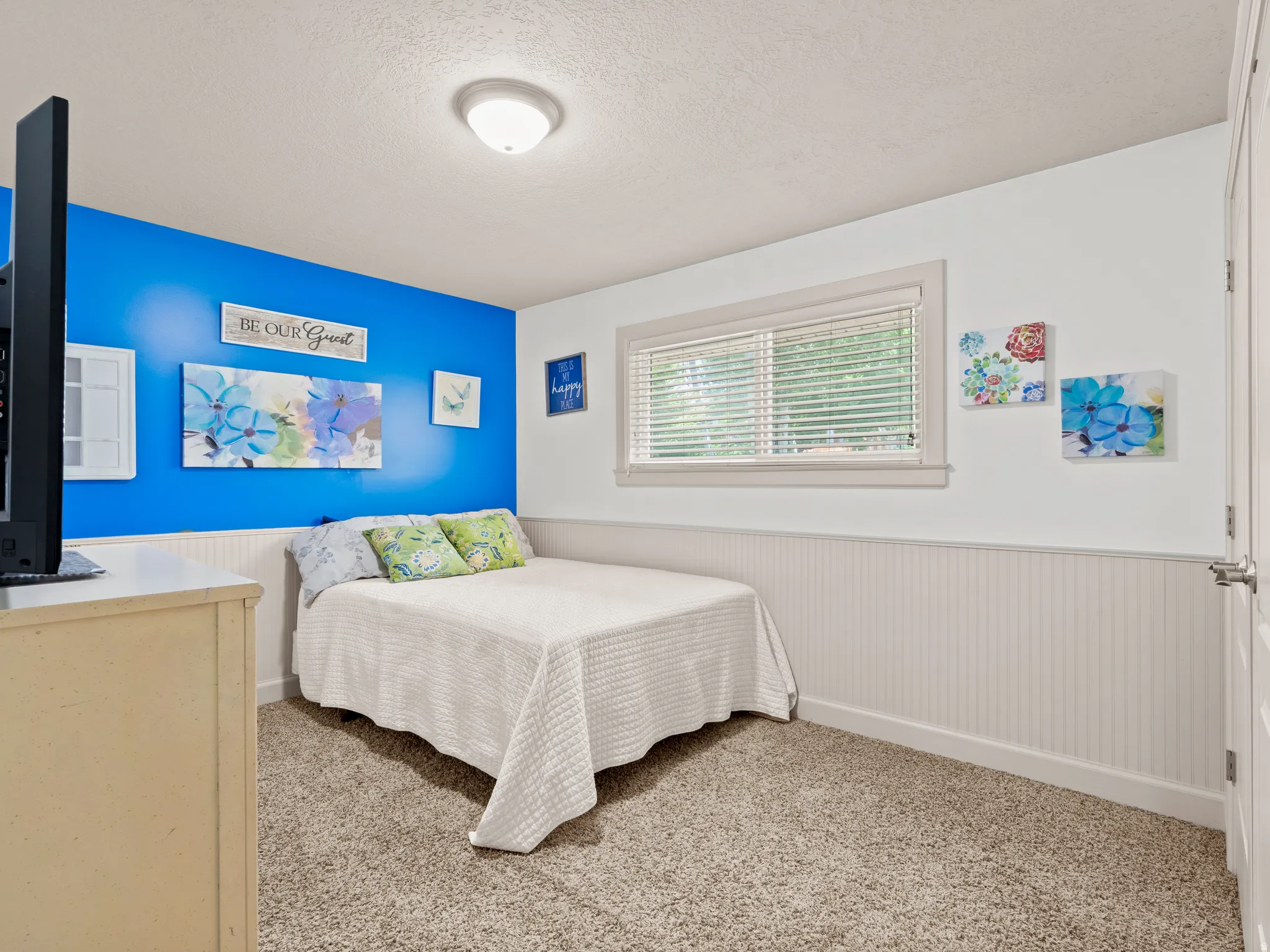 Bedroom featuring a wainscoted wall, a textured ceiling, and light carpet