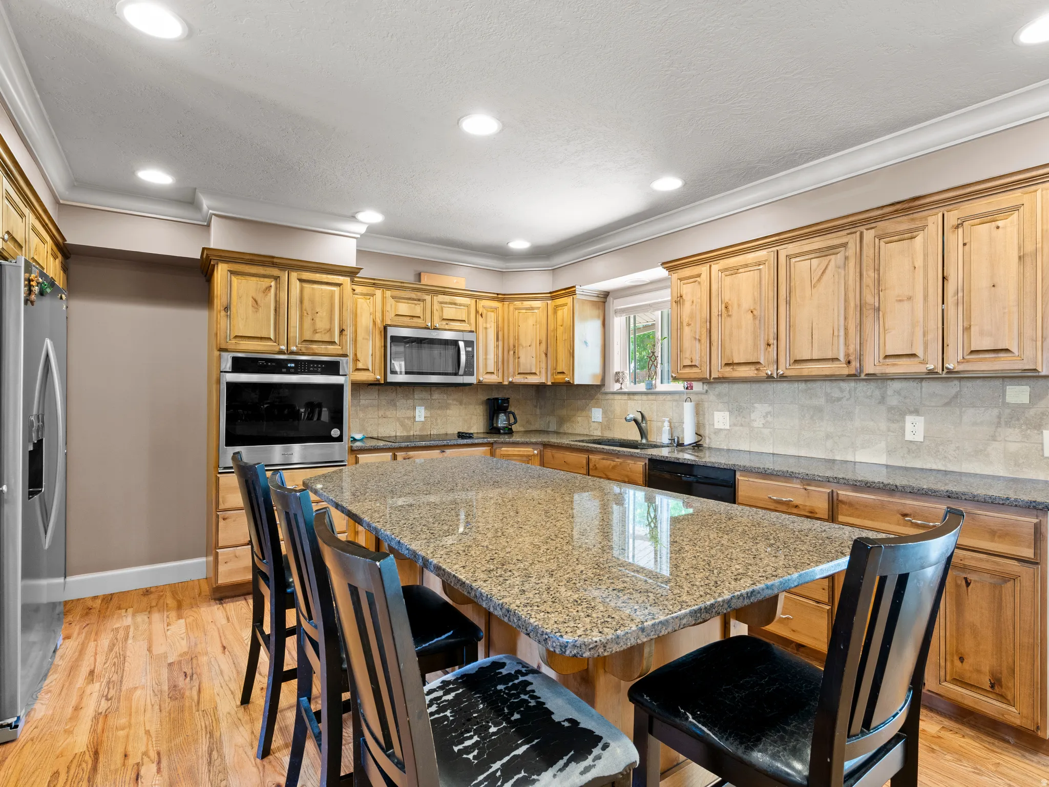 Kitchen featuring a kitchen breakfast bar, dark stone countertops, a kitchen island, black appliances, and light wood-type flooring