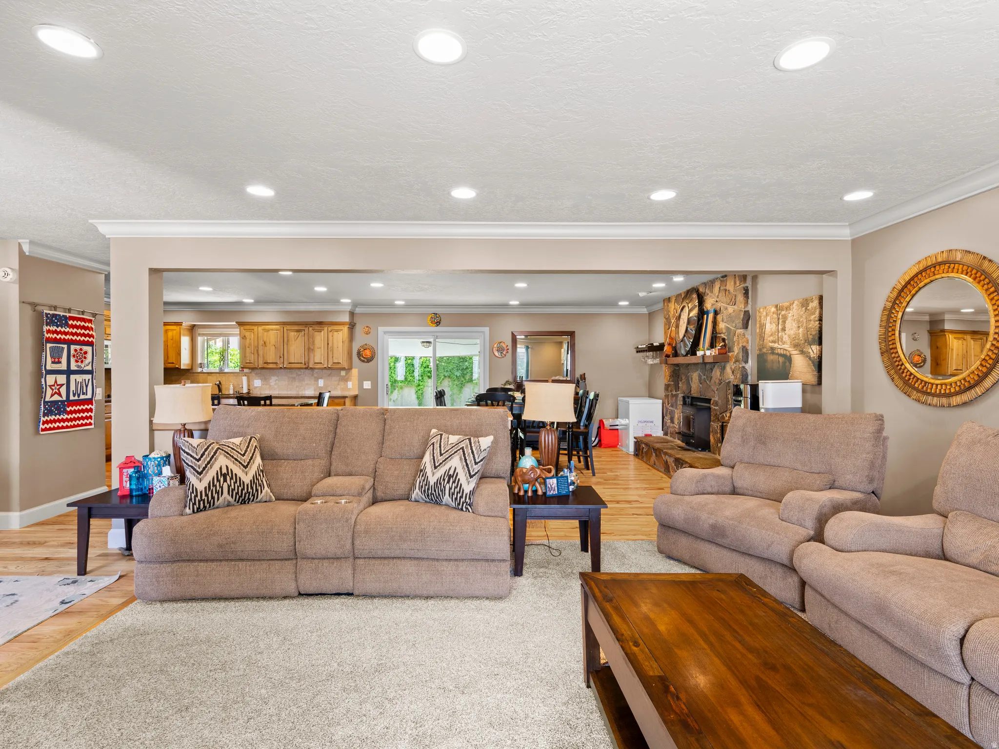 Living room featuring light wood-style floors, a stone fireplace, ornamental molding, and recessed lighting