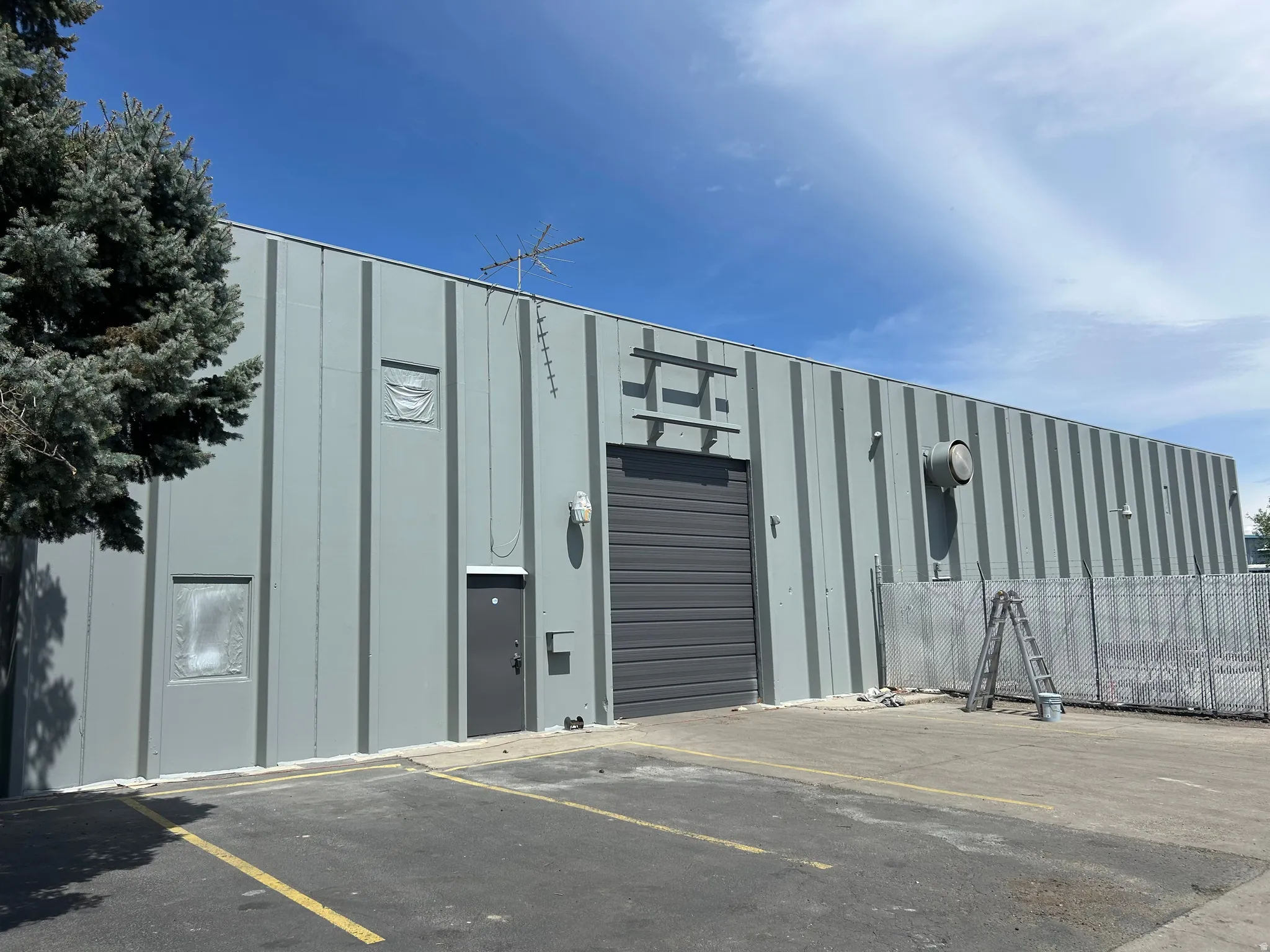 Industrial building featuring a corrugated metal exterior, large roll-up door, paved parking area, and secure chain-link fencing