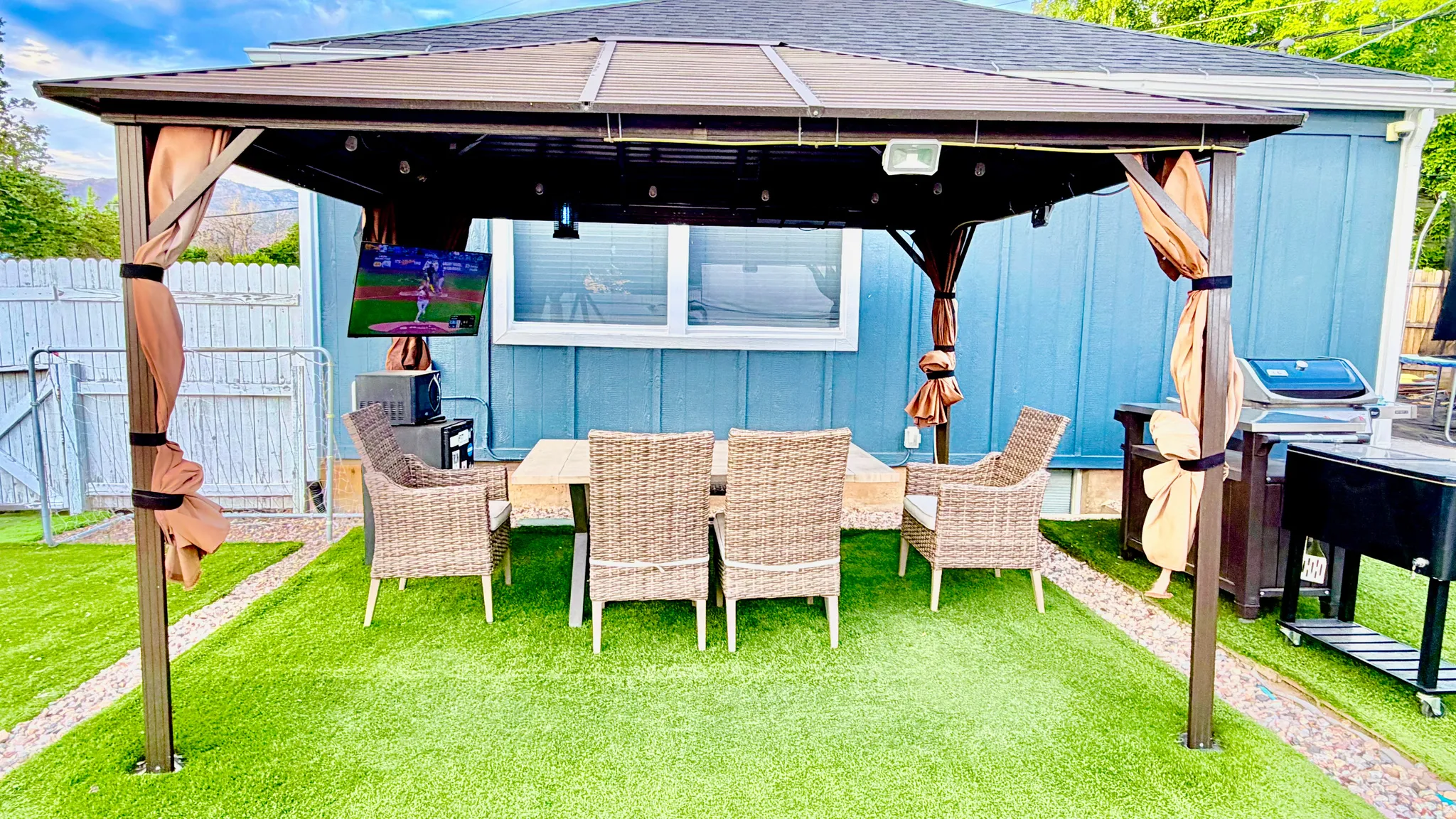 Outdoor gazebo with a hardtop roof and privacy curtains, set on artificial turf