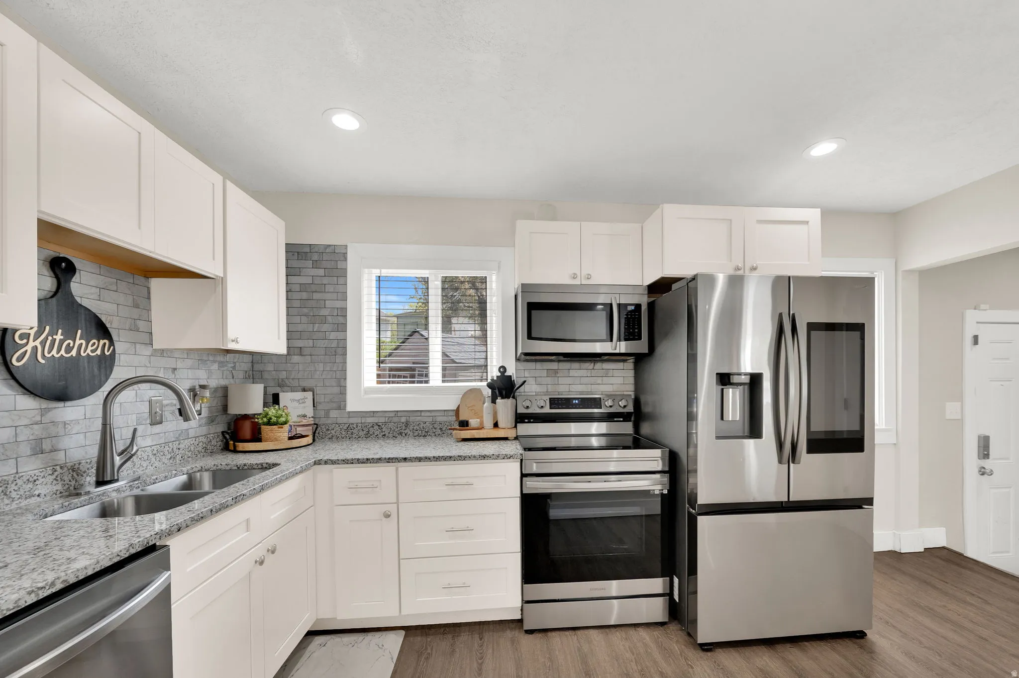 Kitchen with light stone counters, stainless steel appliances, white cabinets, light wood finished floors, and recessed lighting