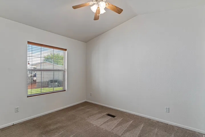 Carpeted primary room featuring a ceiling fan and lofted ceiling