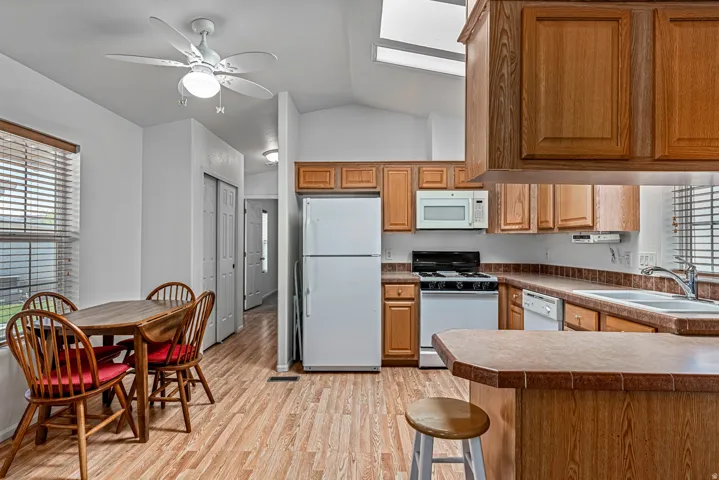 Kitchen featuring white appliances, a peninsula, lofted ceiling, light wood-style floors, and a ceiling fan