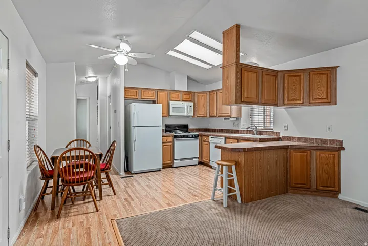 Kitchen with a peninsula, a skylight, wood finish cabinetry, and white appliances
