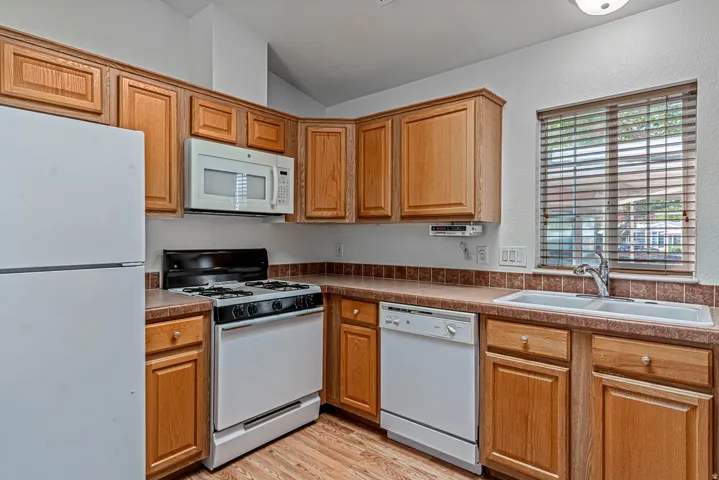 Kitchen with white appliances, light wood-style floors, vaulted ceiling, and wood finish cabinetry