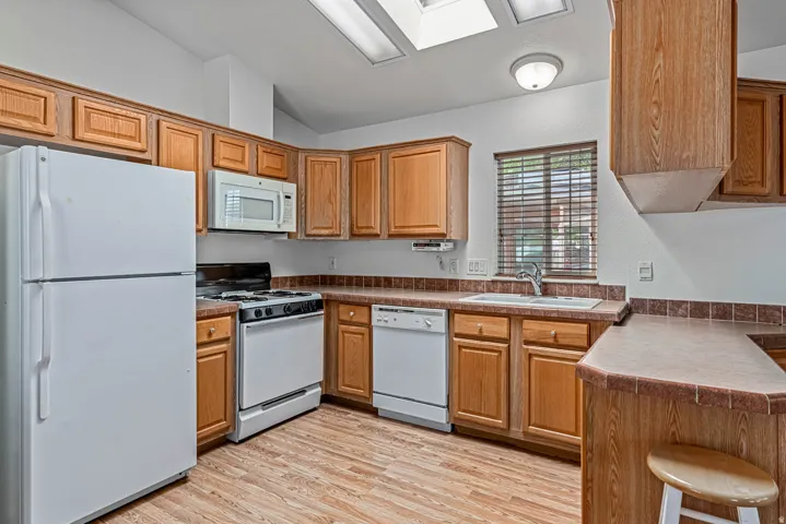 Kitchen featuring white appliances, a peninsula, lofted ceiling, light wood finished floors, and a kitchen breakfast bar