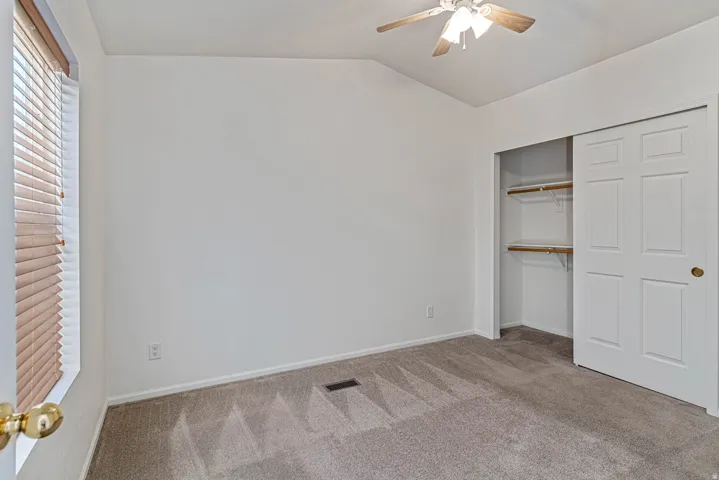 Primary bedroom with light colored carpet, a closet, lofted ceiling, and ceiling fan