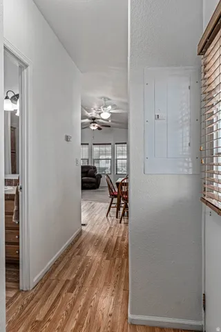 Hallway with a textured wall, electric panel, light wood-style flooring, and a textured ceiling