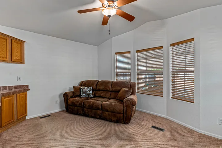 Living room area featuring ceiling fan, lofted ceiling, and light carpet