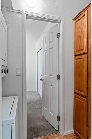 Laundry area featuring a textured wall, stacked washer / drying machine, light wood-style floors, and light carpet