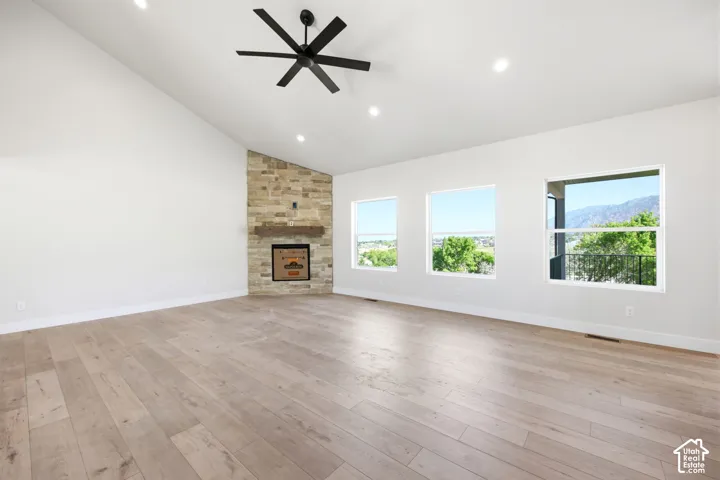 Spacious interior featuring a vaulted ceiling with recessed lighting and a ceiling fan, a stone-clad fireplace with a wood mantel, and wood-finish flooring