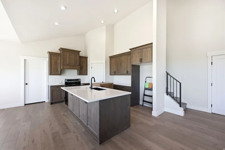 Kitchen featuring a central island with white countertop and integrated sink, wood-finish flooring, dark wood cabinetry with black hardware, and an included range