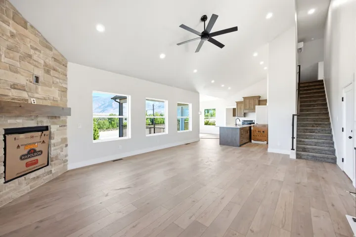 Spacious open-concept living area featuring light wood-finish flooring and a stone-clad fireplace with a wood mantel