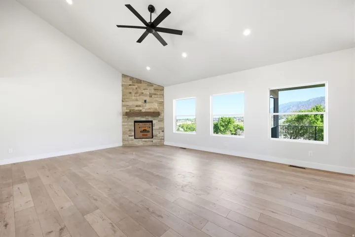 Spacious interior featuring a vaulted ceiling with recessed lighting and a ceiling fan, a stone-clad fireplace with a wood mantel, and wood-finish flooring