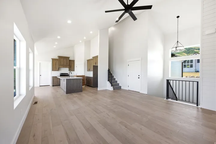 Open concept living area featuring wood-finish flooring, a kitchen with two-toned cabinetry and a center island, vaulted ceilings, and large windows