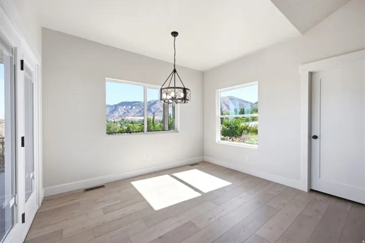 Spacious room featuring light wood-finish flooring, white walls, and a contemporary chandelier