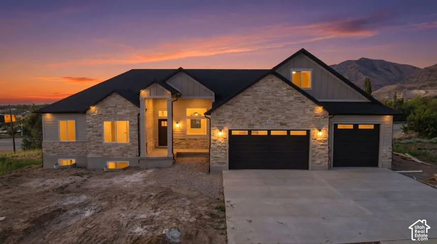 Contemporary residence featuring stone and siding exterior, a dark composite shingle roof, and an attached two-car garage with dark paneled doors