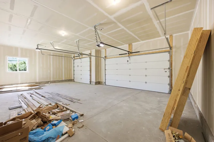 Spacious garage featuring two overhead doors with openers, a large window, concrete flooring, and unfinished drywall