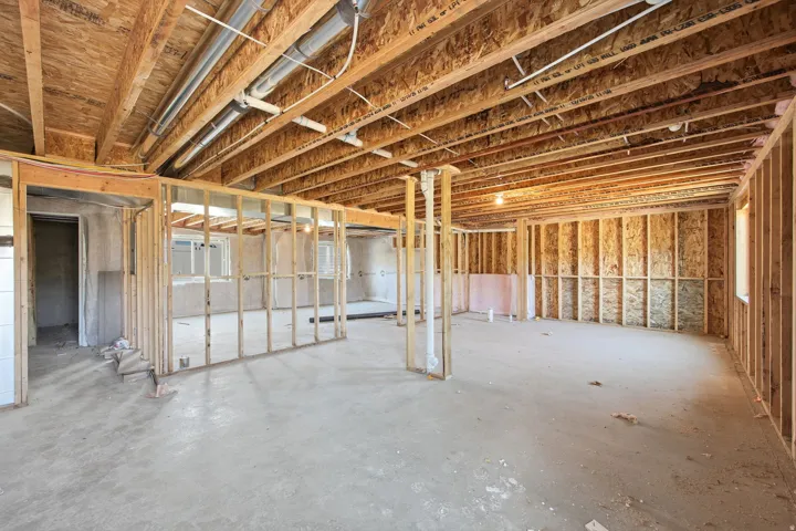 Unfinished basement space featuring exposed wood framing, concrete flooring, visible ceiling joists, and plumbing conduit